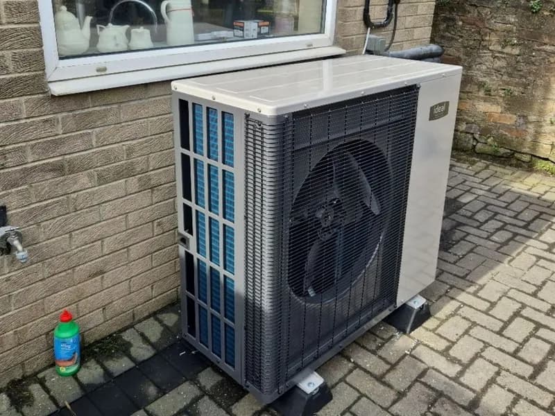 An Ideal air source heat pump on block paving beside a buff brick house