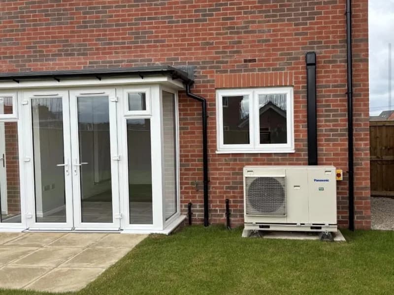 A Panasonic air source heat pump on a slab beside a red brick new build home