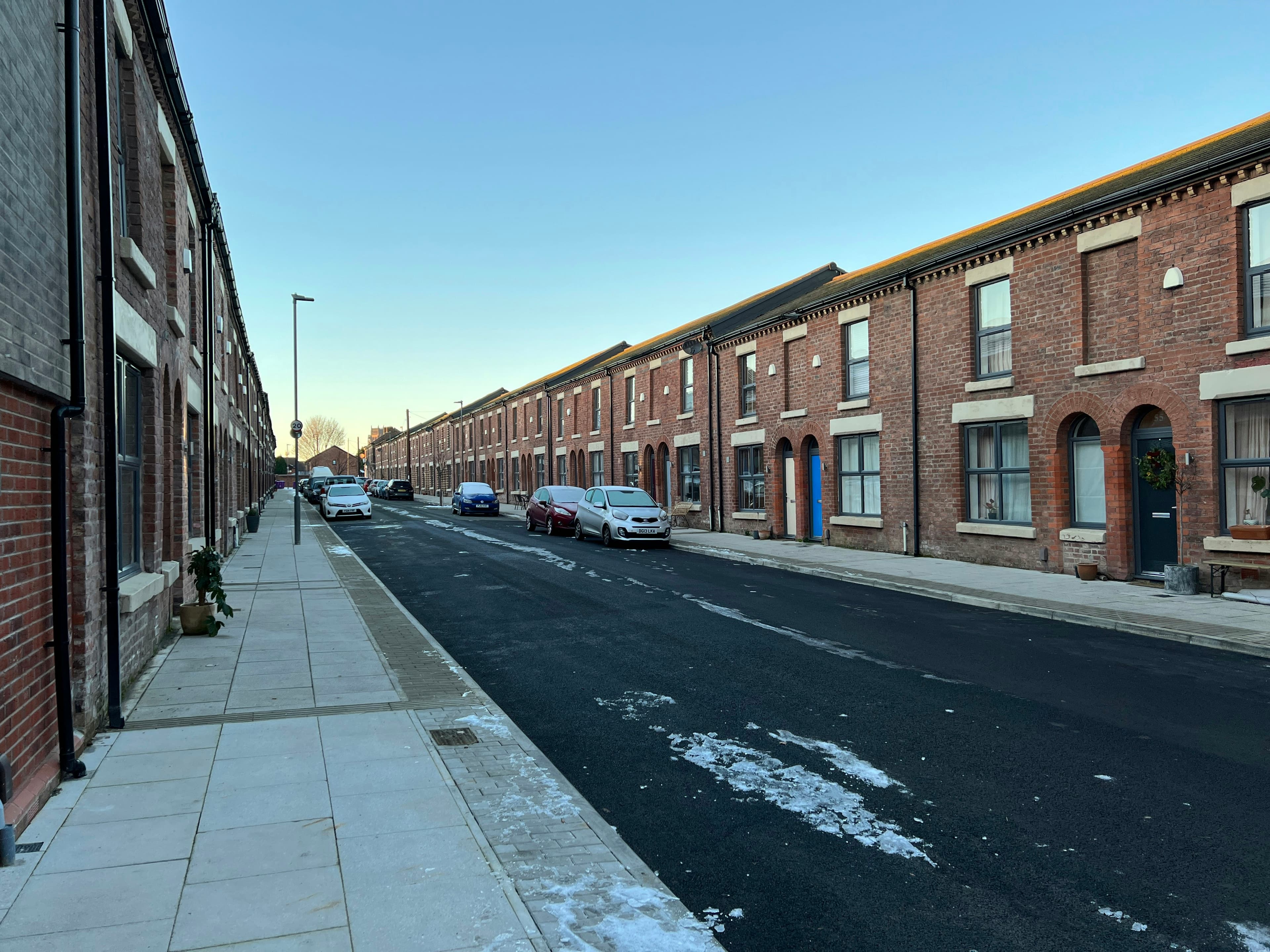 A street lined with brick terraced houses and parked cars
